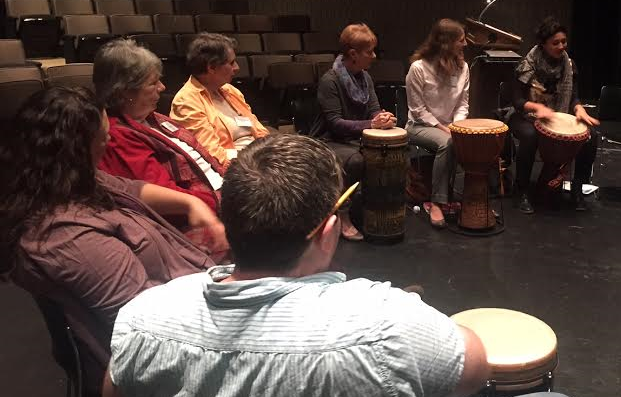 A group of 7 people participate in a drum circle as they learn about incorporating music into programs.