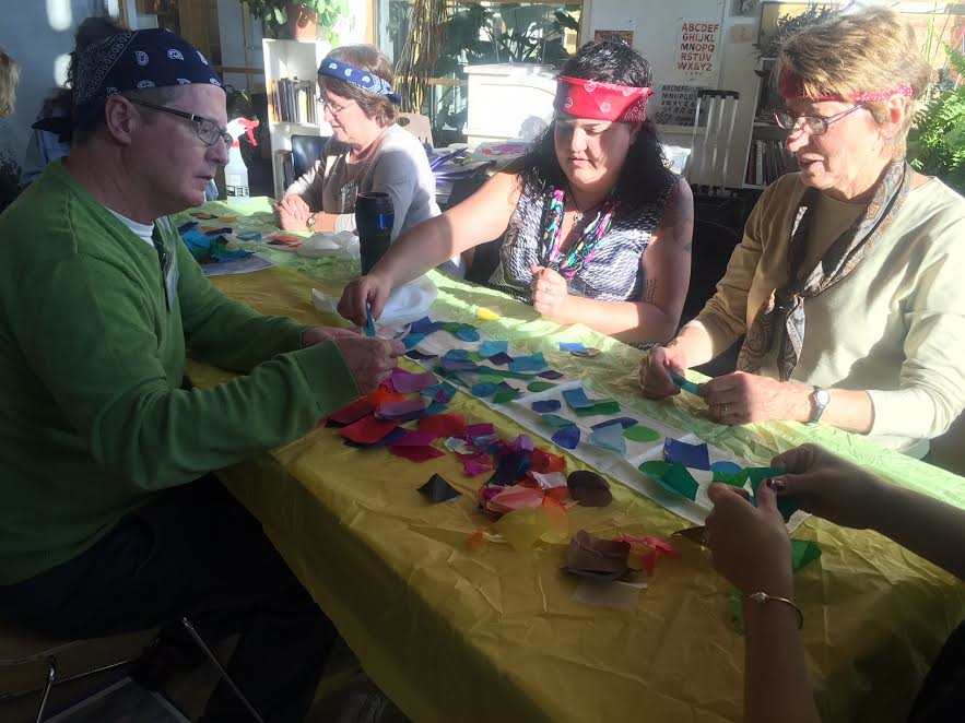 Four 2016 attendees work together on laying pieces of tissue paper on a silk scarf to create a colorful finished dyed scaft.